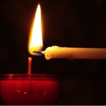 Ein Teelicht wird mit einer Stabkerze angezündet.